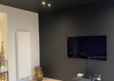 Moderne woonkamer met zwarte muren en plafond, ingebouwde spots en een minimalistische tv-hoek.