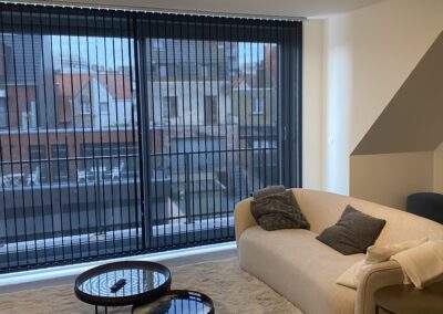 Stijlvolle woonkamer met strakke schilderafwerking, donkere verticale lamellen en een gezellige zithoek.